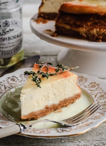 A slice of Goats Cheese, Honey and Thyme Cheesecake on a plate next to a pot of honey and the whole cheesecake