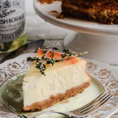A slice of Goats Cheese, Honey and Thyme Cheesecake on a plate next to a pot of honey and the whole cheesecake