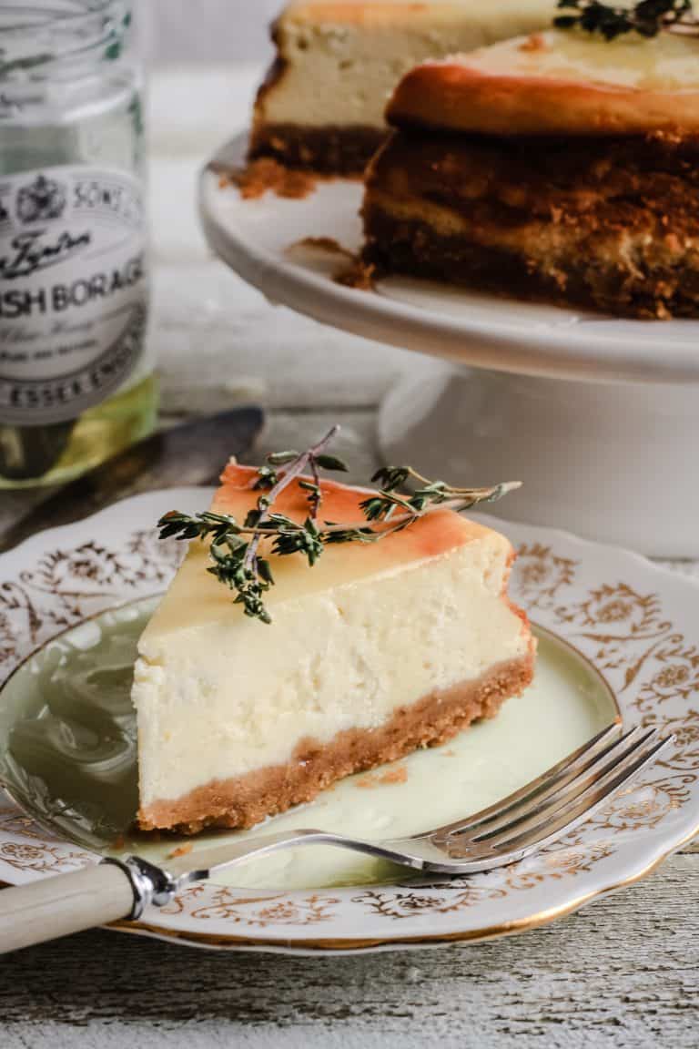 A slice of Goats Cheese, Honey and Thyme Cheesecake on a plate next to a pot of honey and the whole cheesecake