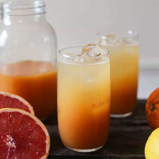 glasses of shrub surrounded by citrus fruit