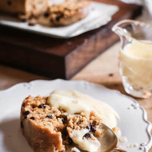A piece of spotted dick on a plate with custard and a spoon