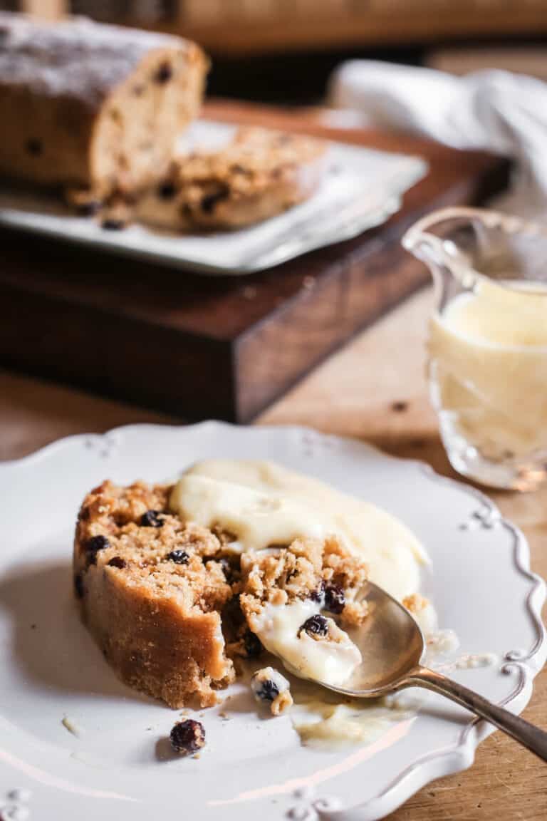 A piece of spotted dick on a plate with custard and a spoon