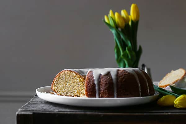 A cut bundt cake with icing dripping on a plate next to flowers