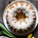 Bundt cake with icing dripping on a plate next to flower