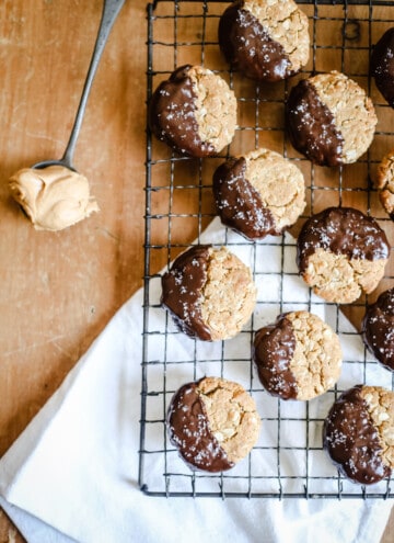 Gluten-Free Chocolate-Dipped Oat Peanut Butter Cookies on a wire rack next to a spoon of peanut butter