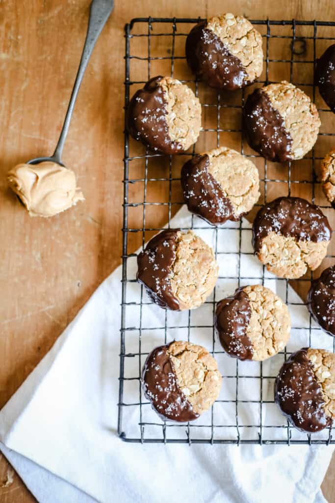 Gluten-Free Chocolate-Dipped Oat Peanut Butter Cookies on a wire rack next to a spoon of peanut butter