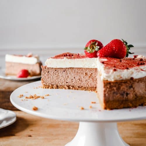 strawberry cheesecake on a cake stand with slices cut out of it. Plates of cheesecake surrounding it.