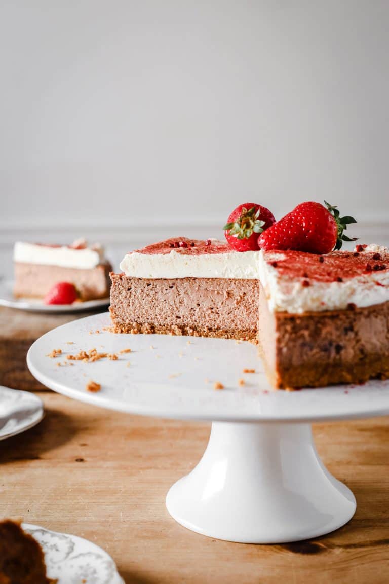 strawberry cheesecake on a cake stand with slices cut out of it. Plates of cheesecake surrounding it.