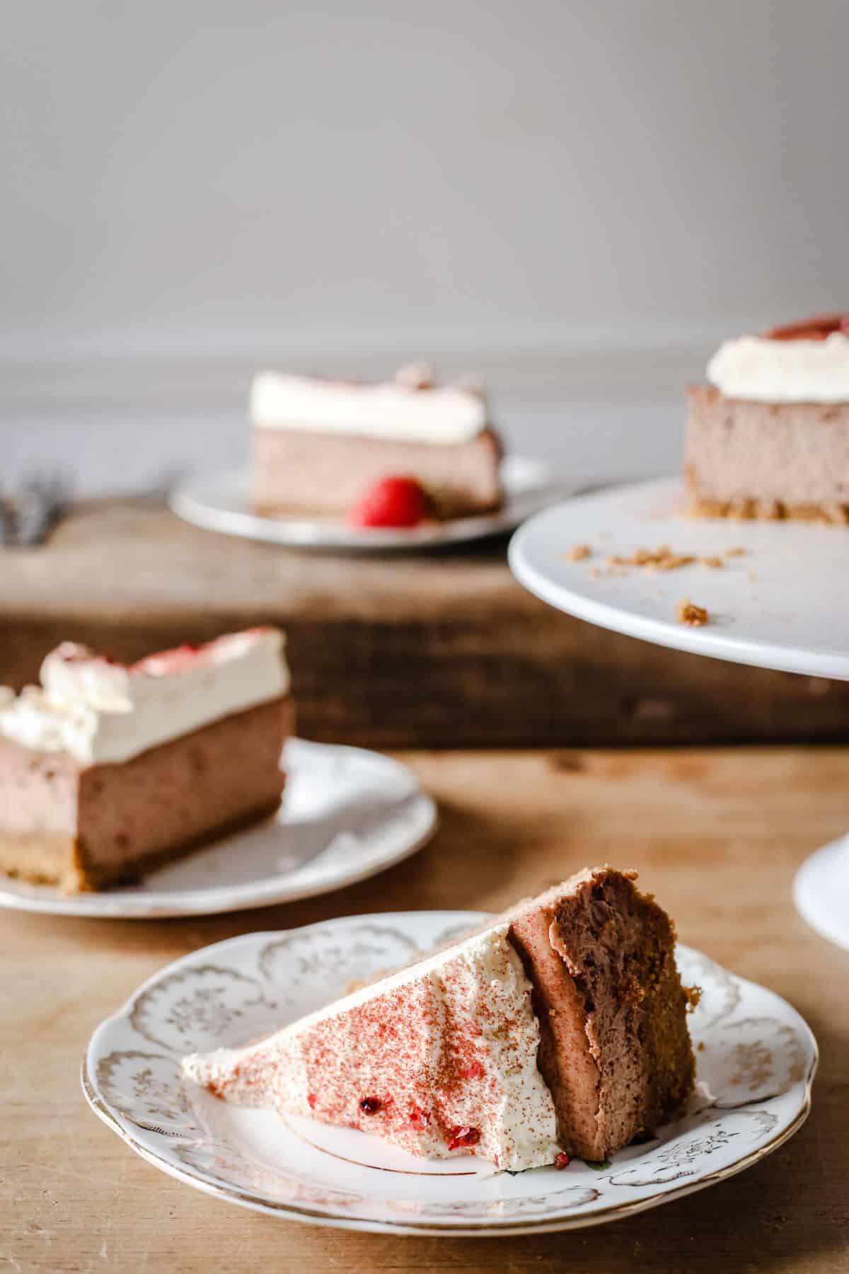 A slice of Strawberry Pink Peppercorn Cheesecake on a plate in the front of the image with plates of cheesecake behind
