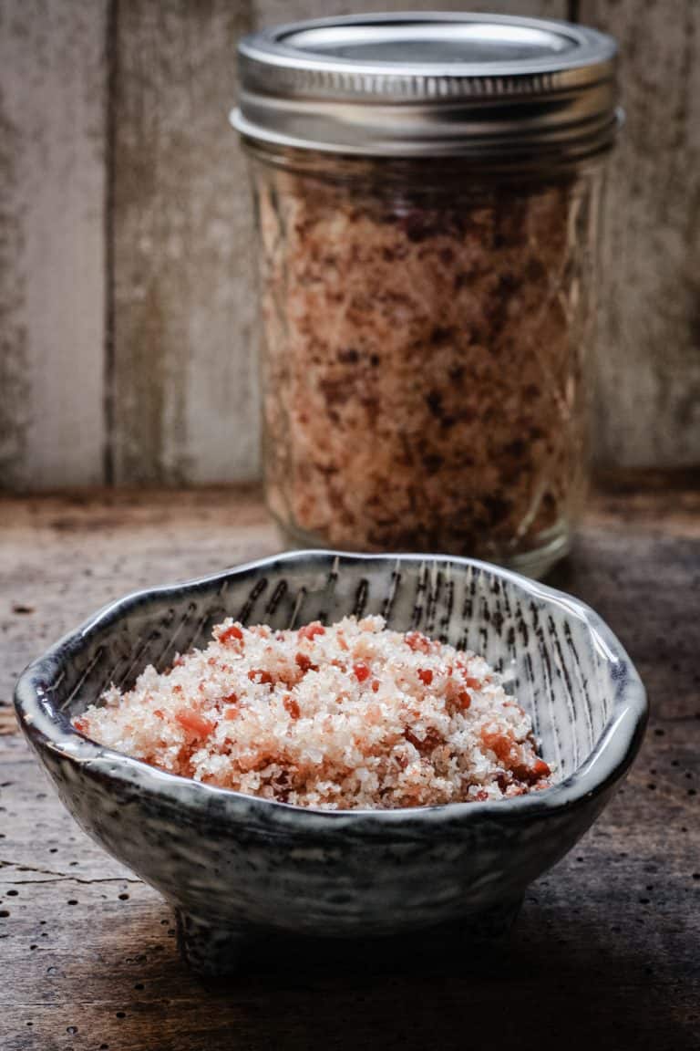 A small bowl of bacon salt in front of a jar of bacon salt