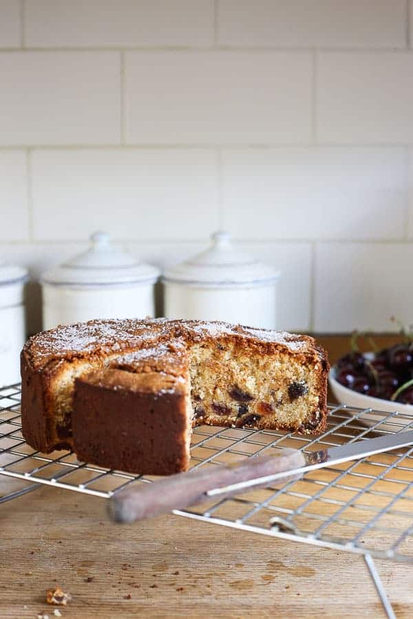 Cherry Cake on a cooling rack with a cake knife sitting in front of a bowl of cherries