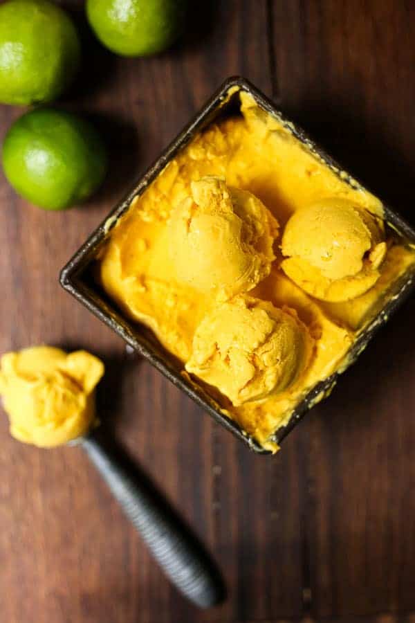 mango fro yo in a bowl next to spoon of it and limes