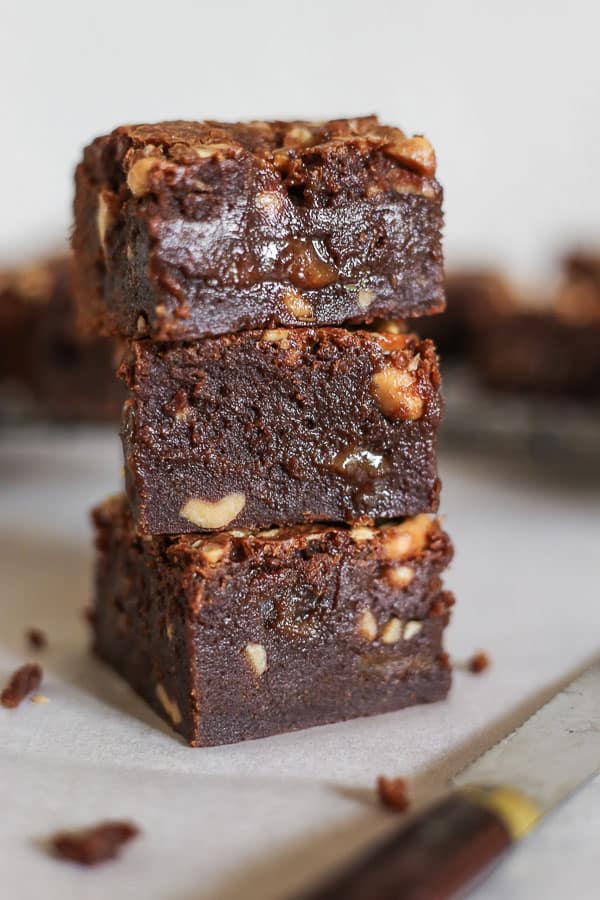 A stack of Milk Chocolate Peanut Caramel Brownies with a knife in front of a wire rack with brownies