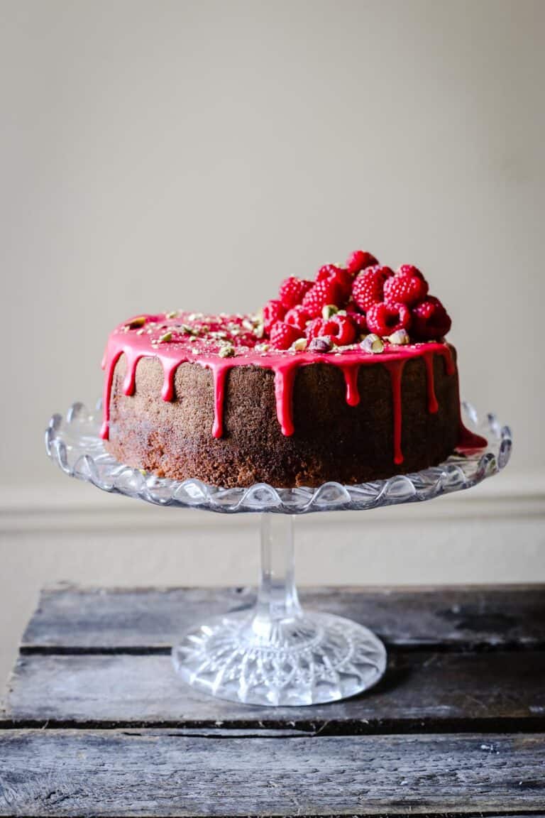 Raspberry Pistachio Cake sitting on a cake stand on a wooden table