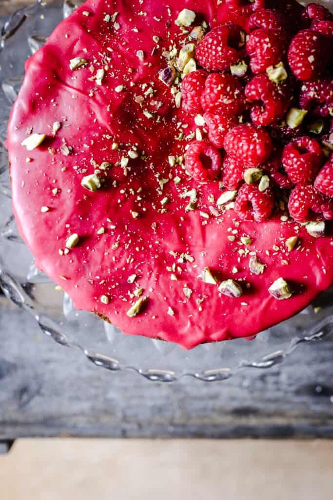 Raspberry Pistachio Cake sitting on a cake stand on a wooden table