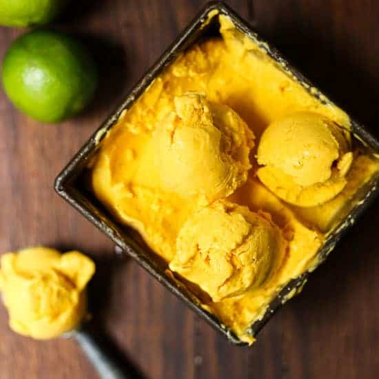 mango fro yo in a bowl next to spoon of it and limes