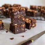 A stack of Milk Chocolate Peanut Caramel Brownies with a knife in front of a wire rack with brownies