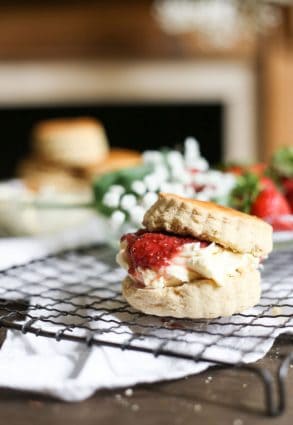 Side shot of a gluten-free scone filled with clotted cream and strawberry jam on a wire rack