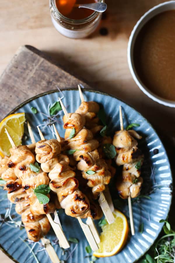 Honey Orange & White Wine Chicken Skewers on a plate with oranges, microherbs next to a bowl of marinade and a jar of honey