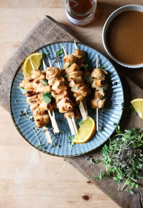 Honey Orange & White Wine Chicken Skewers on a plate with oranges, microherbs next to a bowl of marinade and a jar of honey