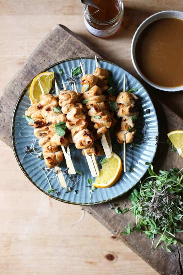 Honey Orange & White Wine Chicken Skewers on a plate with oranges, microherbs next to a bowl of marinade and a jar of honey
