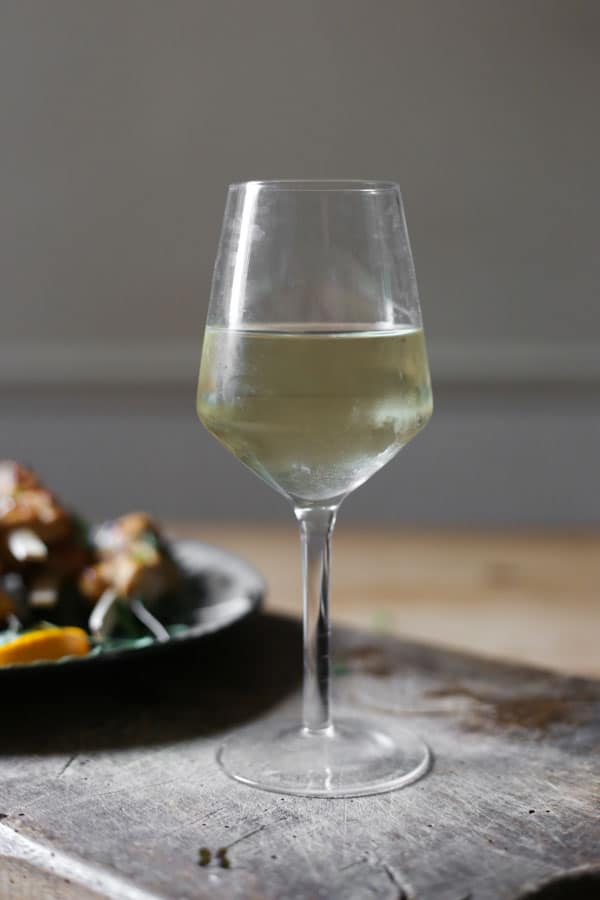 glass of wine on a wooden board next to a plate of food