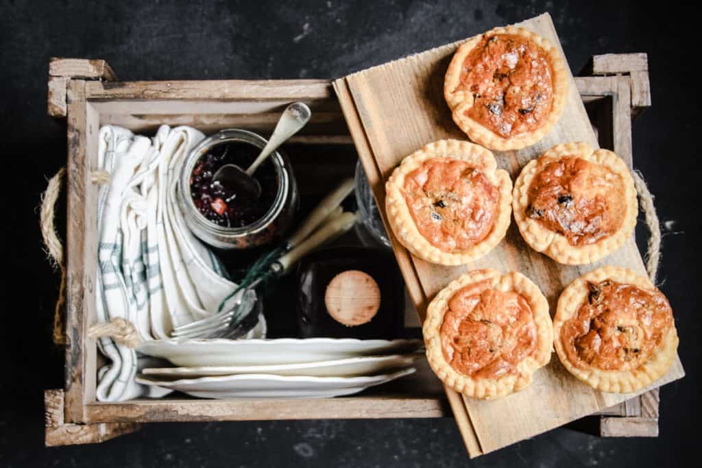 Tartlets on a board balanced on a picnic box with plates and picnicware