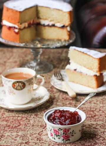 A ramekin of jam on a table next to tea and cake
