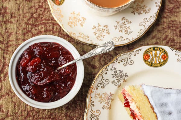 A ramekin of jam on a table next to tea and cake