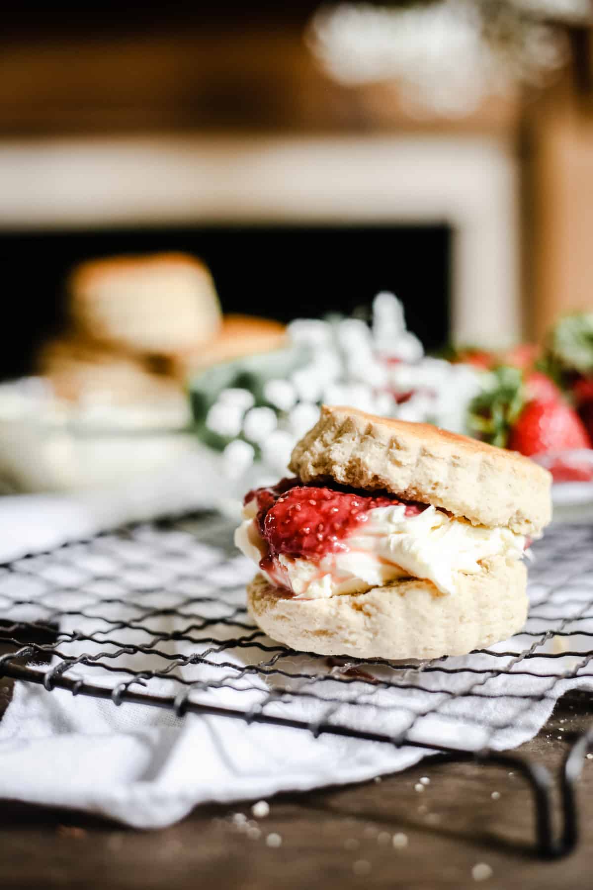 Side shot of a gluten-free scone filled with clotted cream and strawberry jam on a wire rack