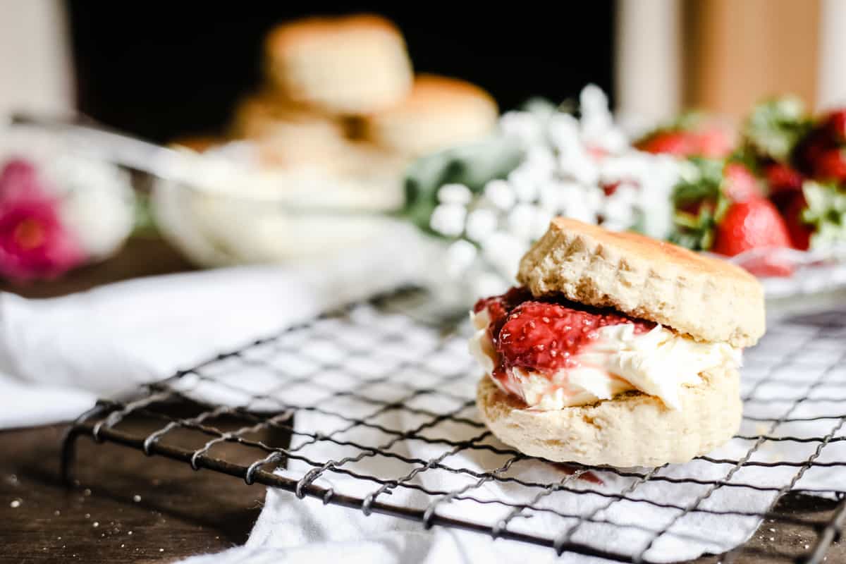 Side shot of a gluten-free scone filled with clotted cream and strawberry jam on a wire rack