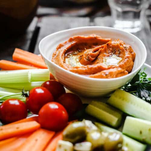 A bowl of Cumin Whipped Butternut Squash and Red Pepper Dip on a plate of crudites