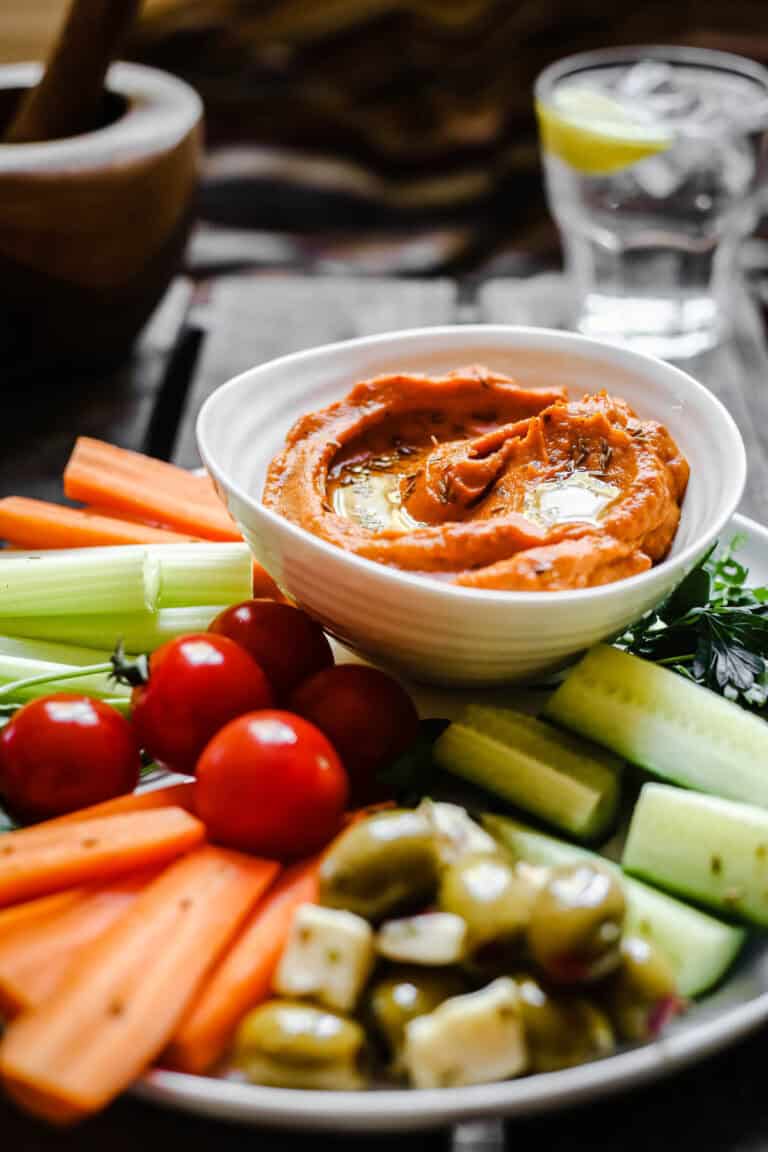 A bowl of Cumin Whipped Butternut Squash and Red Pepper Dip on a plate of crudites