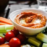 A bowl of Cumin Whipped Butternut Squash and Red Pepper Dip on a plate of crudites