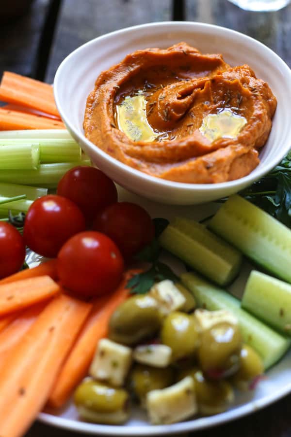 A bowl of Cumin Whipped Butternut Squash and Red Pepper Dip on a plate of crudites