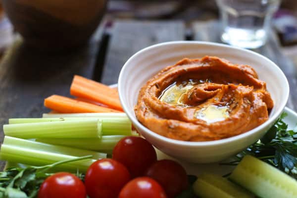 A bowl of Cumin Whipped Butternut Squash and Red Pepper Dip on a plate of crudites