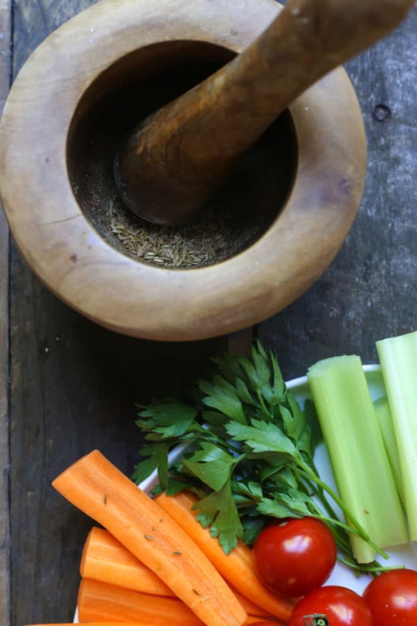 A pestle and mortar filled with cumin seeds next to a plate of crudites