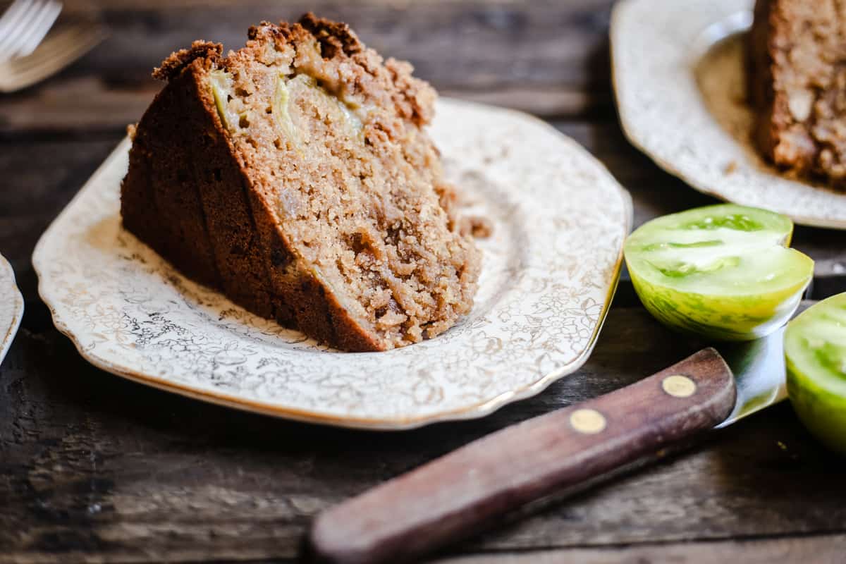 side shot of a slice of Green Tomato and Stem Ginger Cake with Streusel Topping {gluten-free} on a plate with green tomatoes next to it