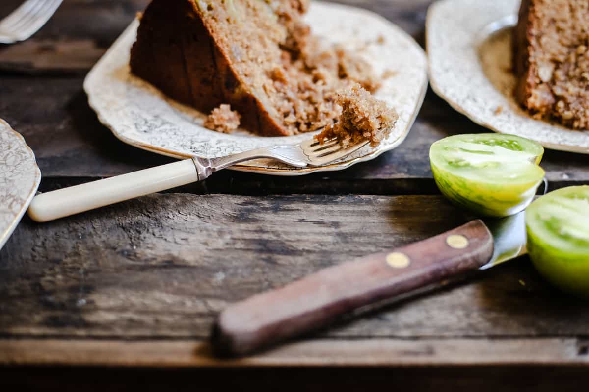 side shot of a slice of Green Tomato and Stem Ginger Cake with Streusel Topping {gluten-free} on a plate with green tomatoes next to it