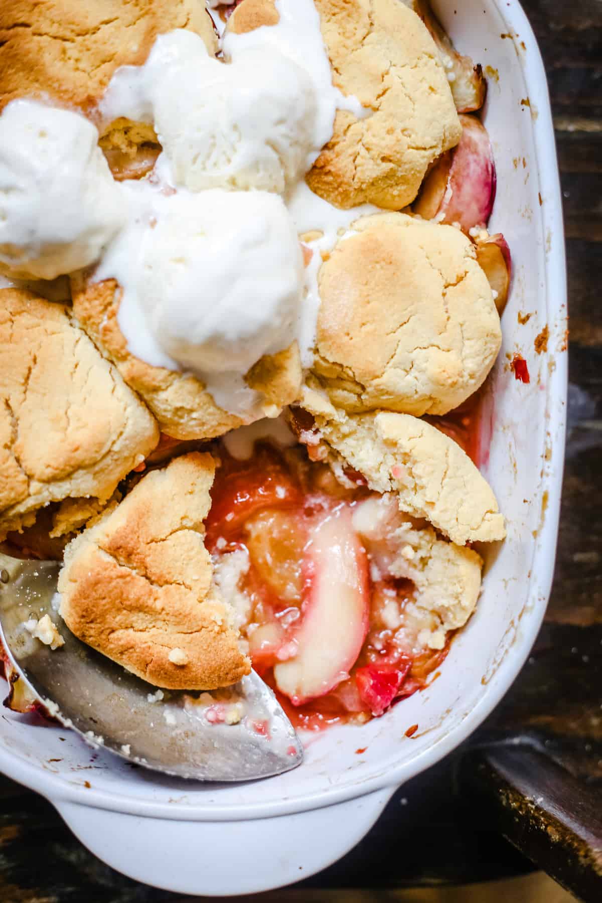 overhead shot of a baking dish of plum nectarine cornbread cobbler with ice cream and a serving spoon