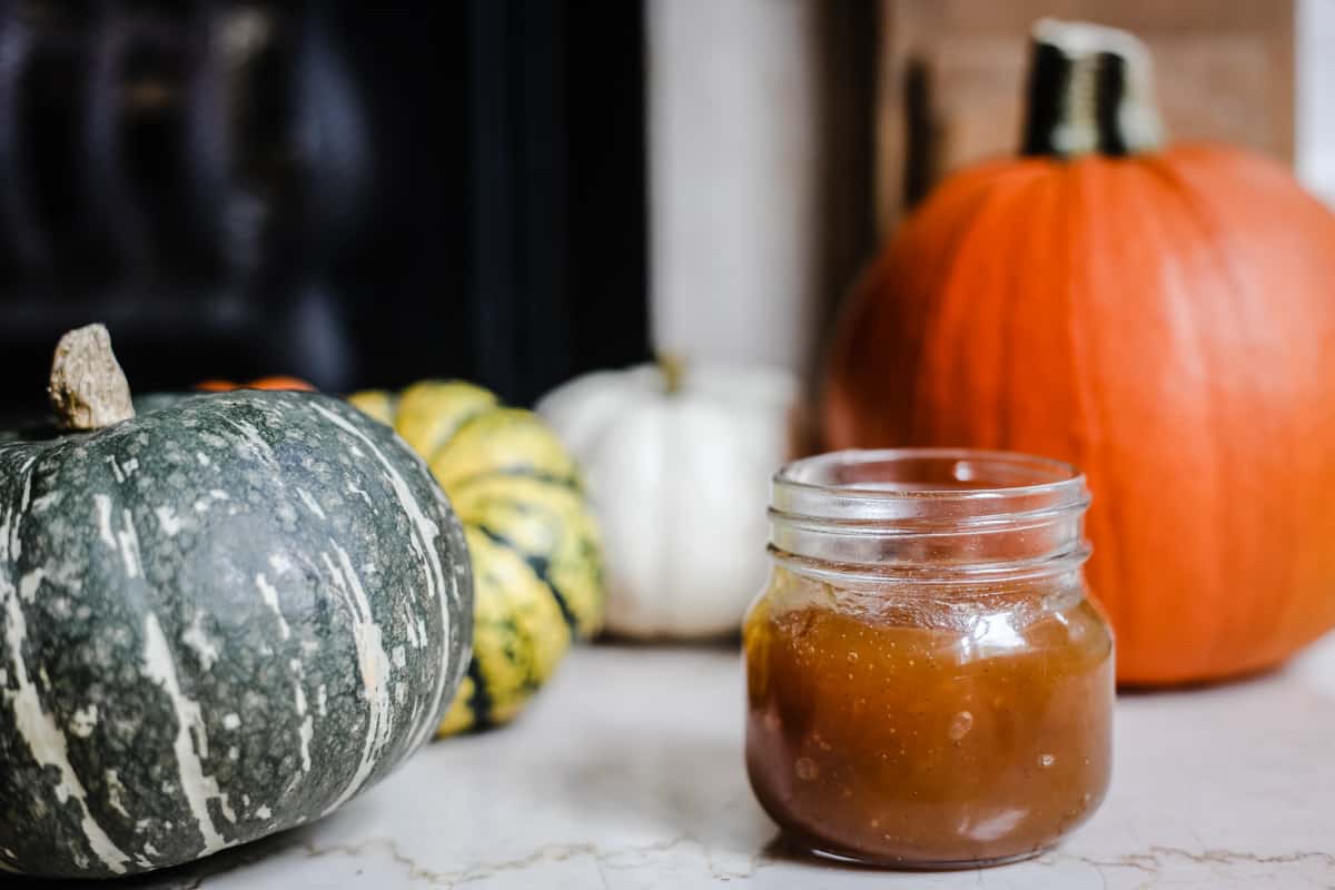 side on shot of pumpkin jam with a spoon in it surrounded by pumpkins