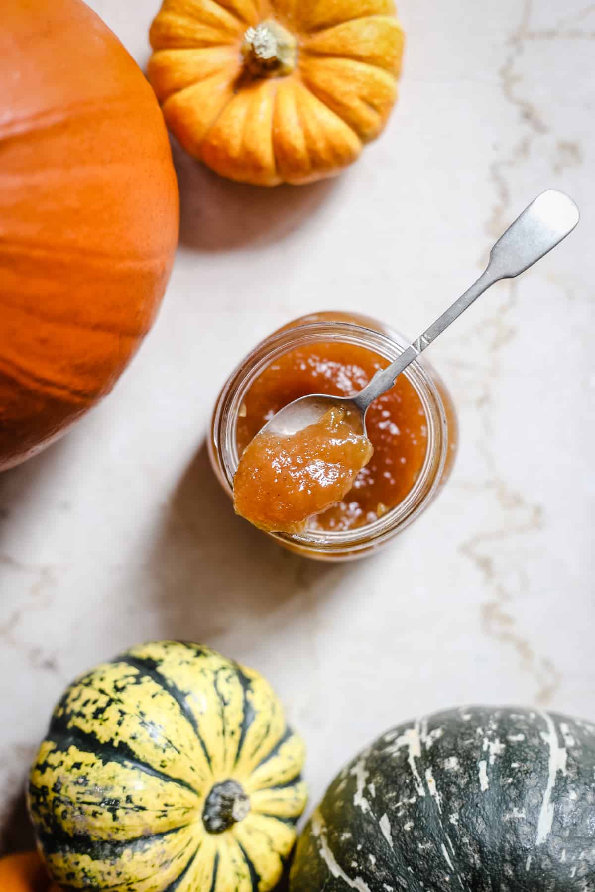 overhead shot of pumpkin jam with a spoon in it surrounded by pumpkins