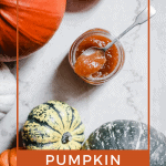 Pumpkin Jam in a pot with a spoon resting on top. Surrounded by pumpkins and squash with text overlay saying Pumpkin Jam