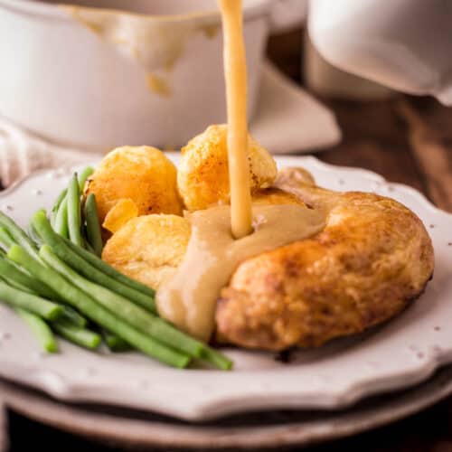 Gluten-Free Gravy being poured out of a gravy boat over a plate of roast chicken and vegetables