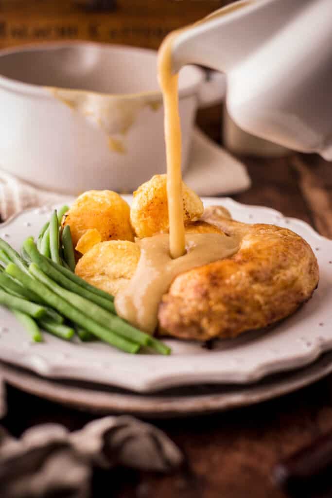 Gluten-Free Gravy being poured out of a gravy boat over a plate of roast chicken and vegetables