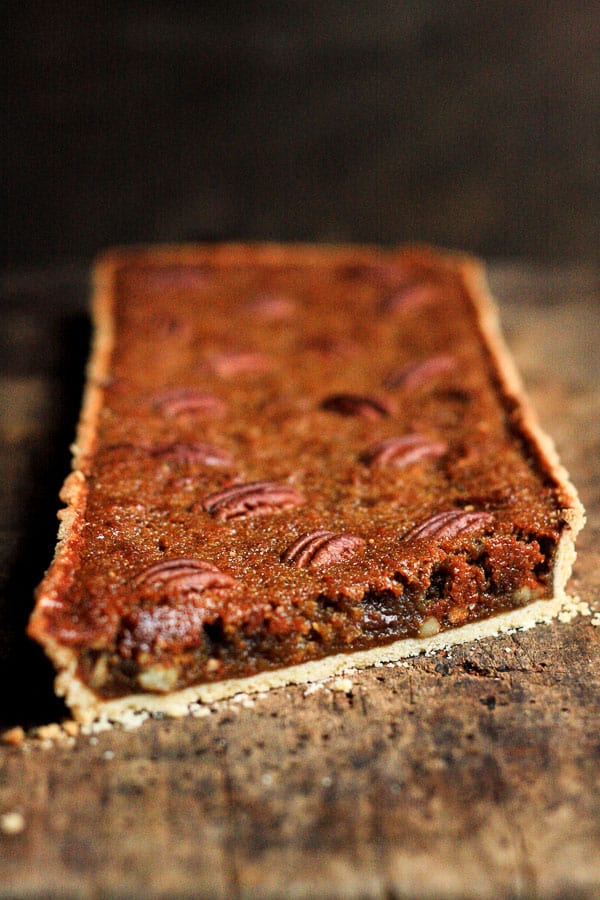 A close up of a sliced pecan treacle tart on wooden table