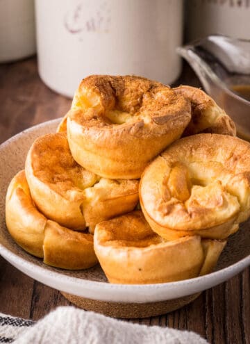Gluten-Free Yorkshire Puddings piled high in a serving bowl on a plate on a wooden table