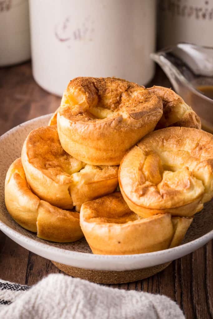Gluten-Free Yorkshire Puddings piled high in a serving bowl on a plate on a wooden table