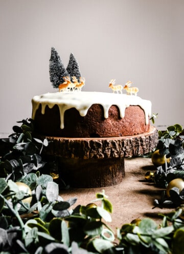 Almond & Mincemeat Christmas Sponge Cake on a cake stand surrounded by greenery