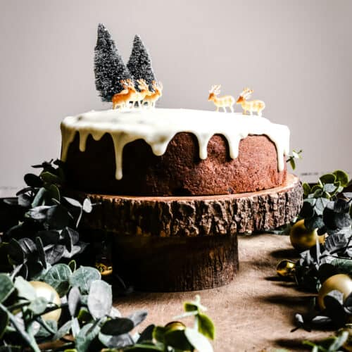 Almond & Mincemeat Christmas Sponge Cake on a cake stand surrounded by greenery